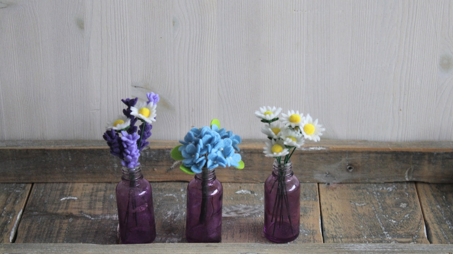 3 boeketjes in kleine glazen vaasjes met madeliefjes/hortensia/lavendel op houten ondergrond en lichte achtergrond