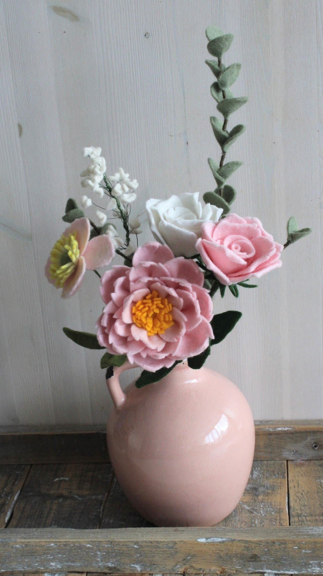 Romantisch boeket van vilt, met gipskruid en roze pioenroos, roze en witte roos, roze anemoon en eucalyptus tak, ideaal voor een bruiloft. of andere gelegenheid Het boeket staat in een roze vaas met een houten ondergrond