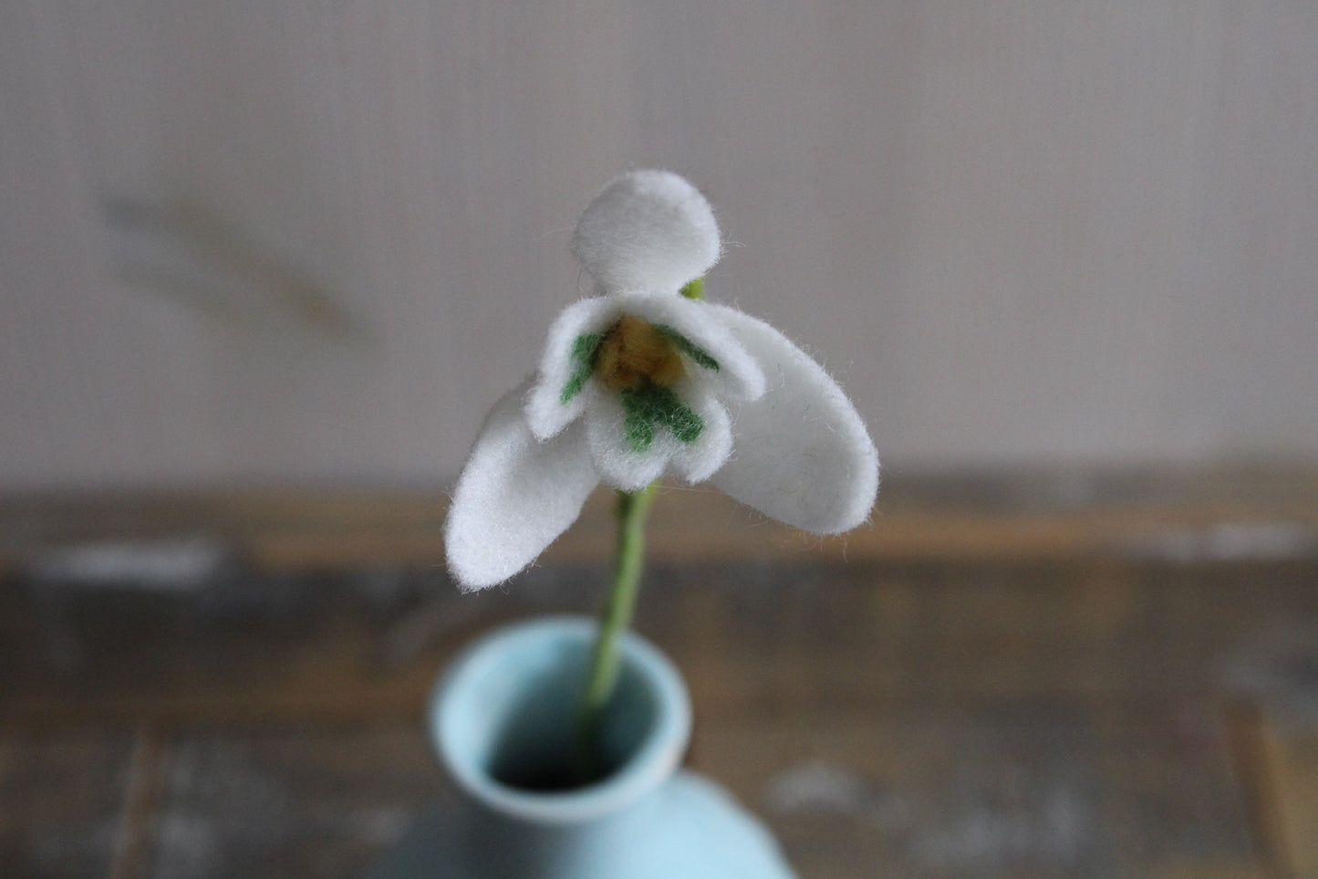 Close-up vilten sneeuwklokje in blauw vaasje op een houten ondergrond
