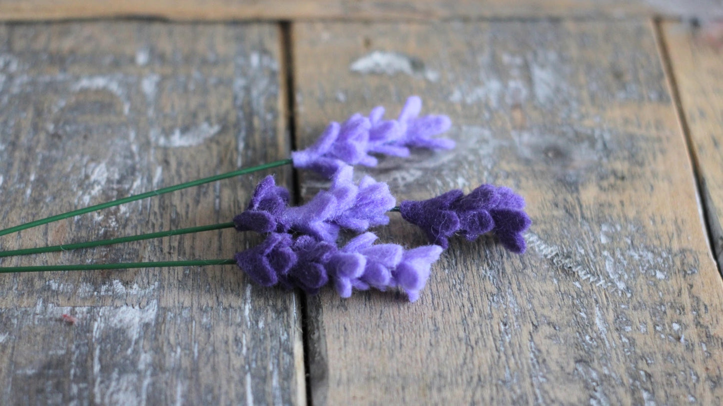 Handgemaakte vilten lavendel als paarse decoratie op een rustieke houten plank.