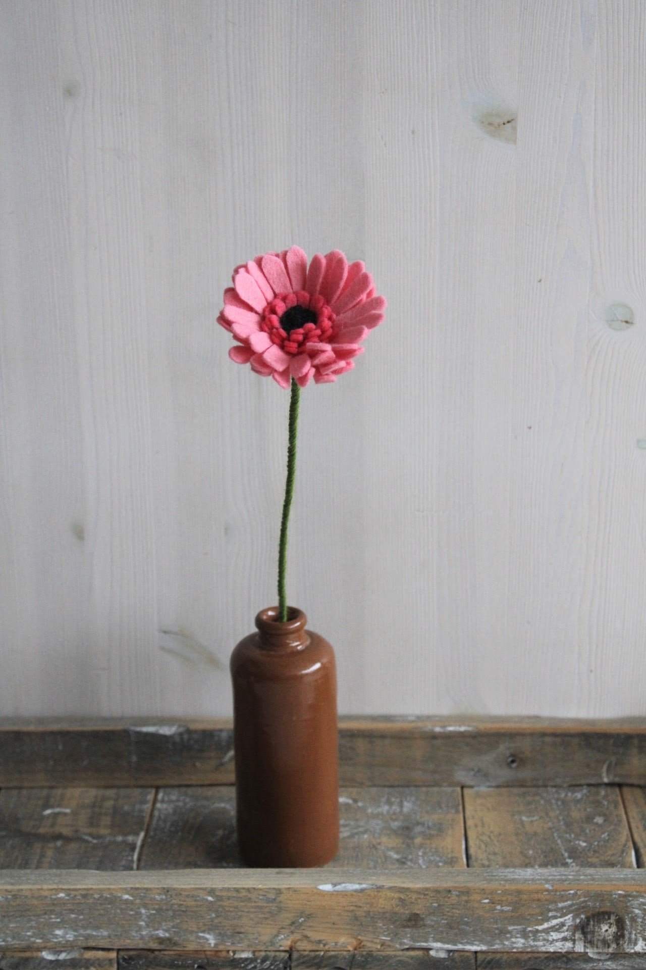 Handgemaakte roze gerbera van vilt in een bruine fles op een houten ondergrond