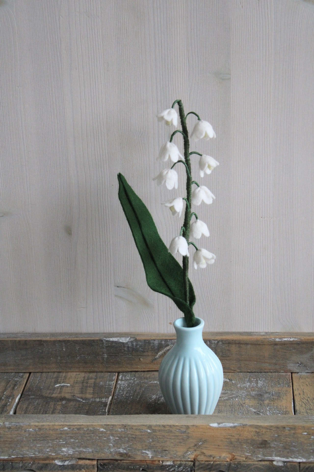 Handgemaakt lelietje-van-dalen van vilt met delicate witte bloemetjes op een rustieke houten ondergrond