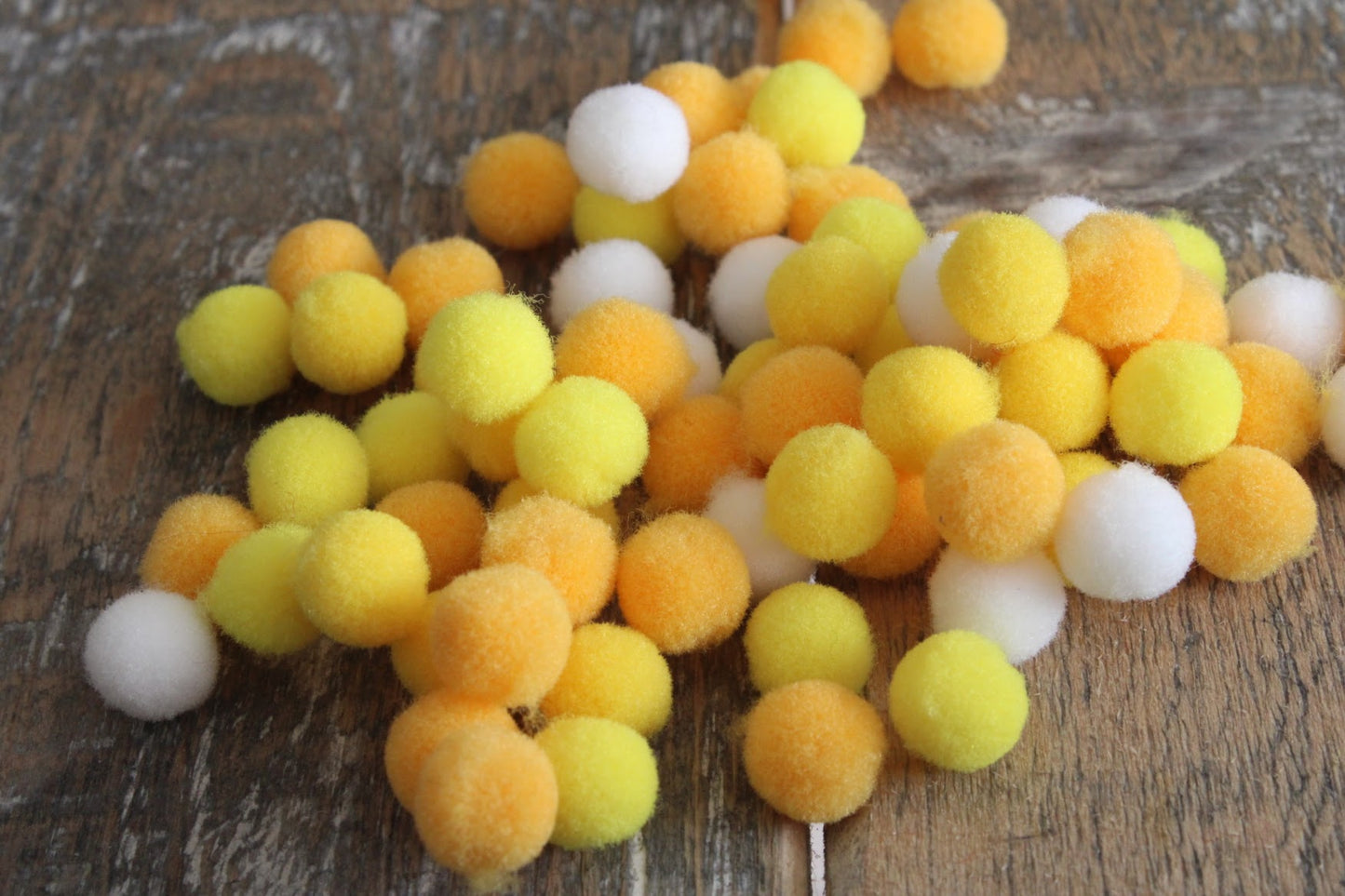 Collectie zachte vilten pompons in de kleuren geel, oranje en wit, gebruikt voor knutselprojecten, op een vintage houten oppervlak.