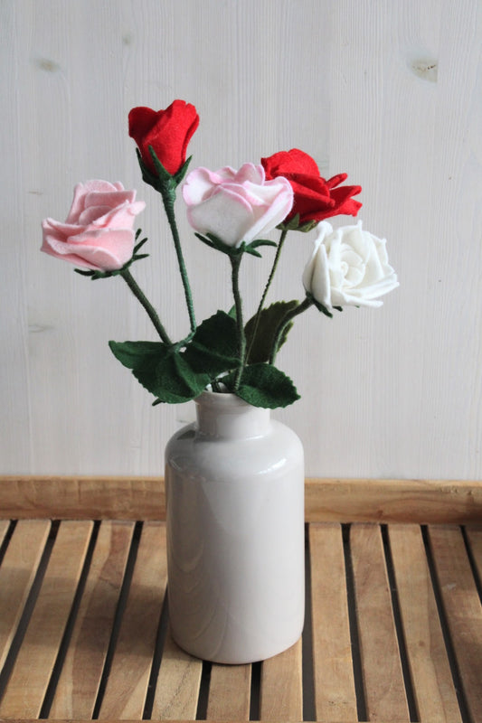 Bosje handgemaakte vilten rozen, in de kleuren rood, roze en wit met blad eraan in een grijze vaas op een houten ondergrond