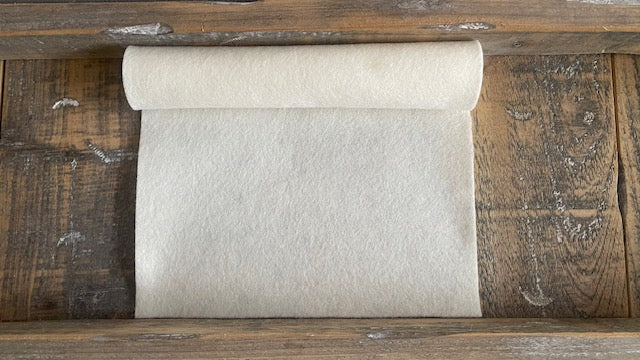 Rolletje wolvilt in de kleur ecru nummer 103 op een houten ondergrond voor het maken van viltbloemen, zoals vilten roos, vilten anemoon, narcis van vilt