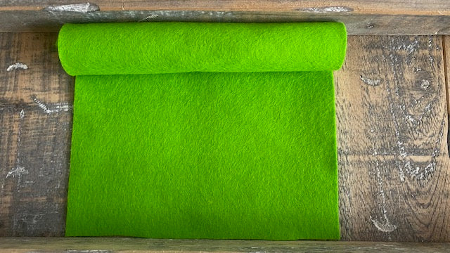 Rolletje wolvilt in de kleur lichtgroen nummer 24 op een houten ondergrond voor het maken van viltbloemen