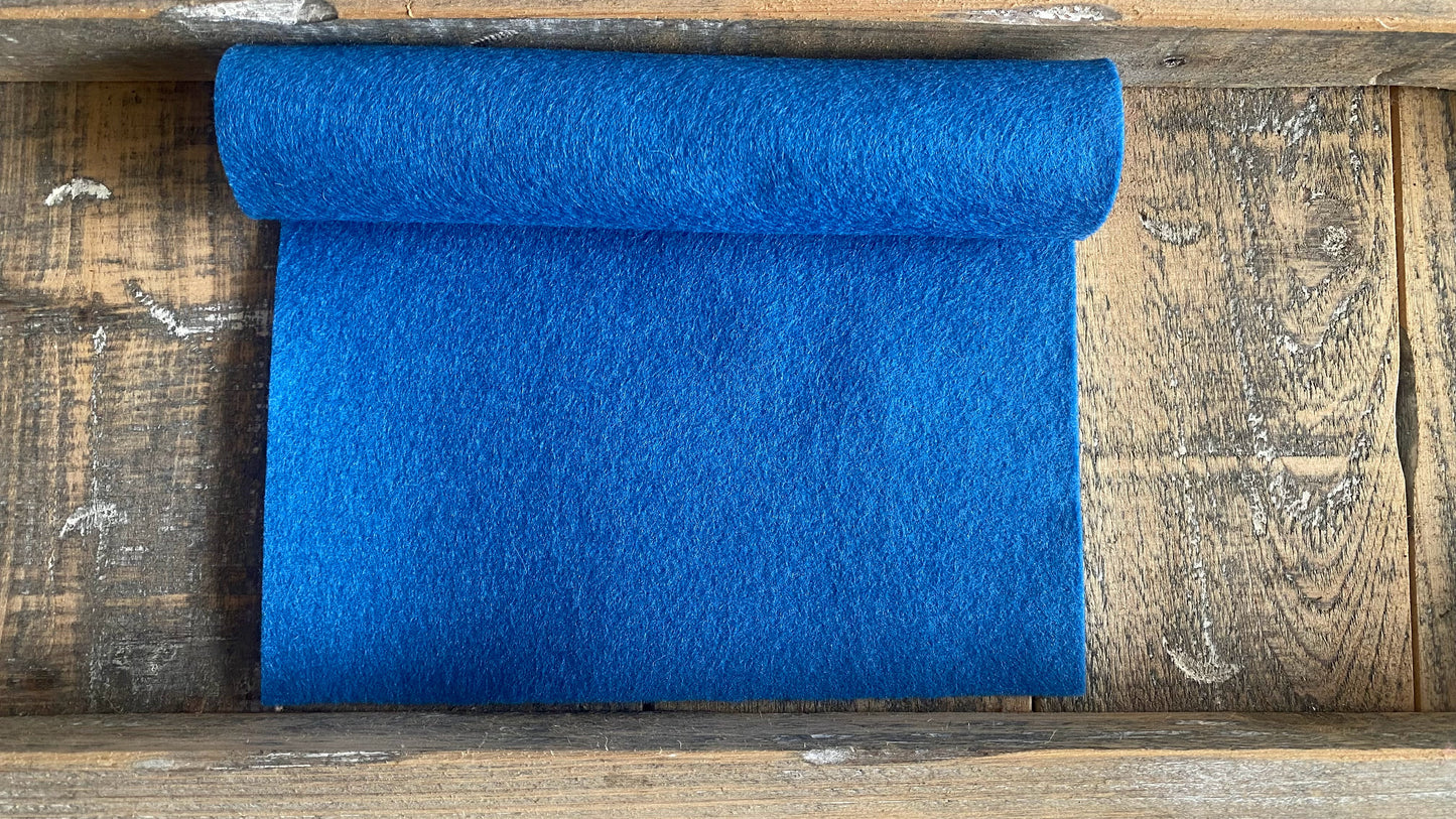 Rolletje wolvilt in de kleur midden blauw nummer 37 op een houten ondergrond voor het maken van viltbloemen, zoals vilten ridderspoor, vilten korenbloem, vilten blauw druifje, hortensia van vilt