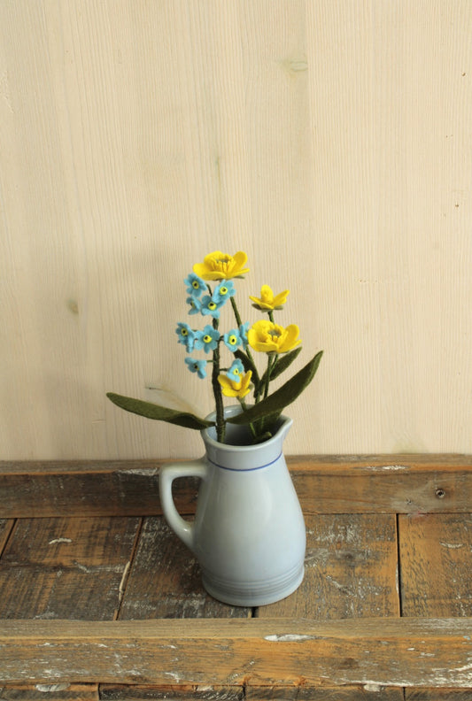 Rustieke blauw-grijze keramieken kan met handvat en subtiele blauwe lijn met vergeet me nietje en boterbloem geplaatst op een houten ondergrond