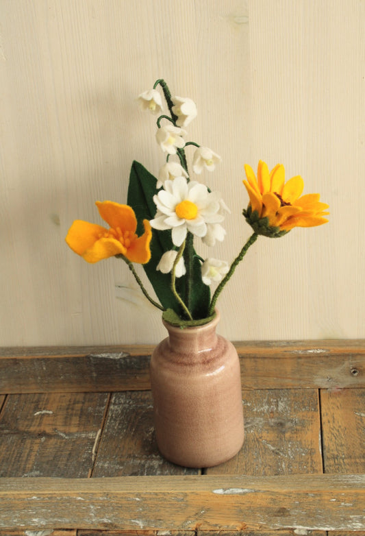 viltbloemenboeketje, klaproos, zonnebloem, margriet, lelietje van dalen in oud roze vaasje op een houten ondergrond