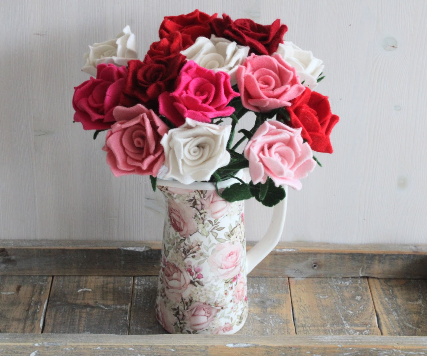 Groot handgemaakt boeket van vilten rozen in verschillende kleuren, met gedetailleerde groene bladeren en stevige stelen in een gebloemde vaas. Een tijdloze en duurzame bloemendecoratie, perfect als romantisch cadeau of sfeervolle interieuraccessoire