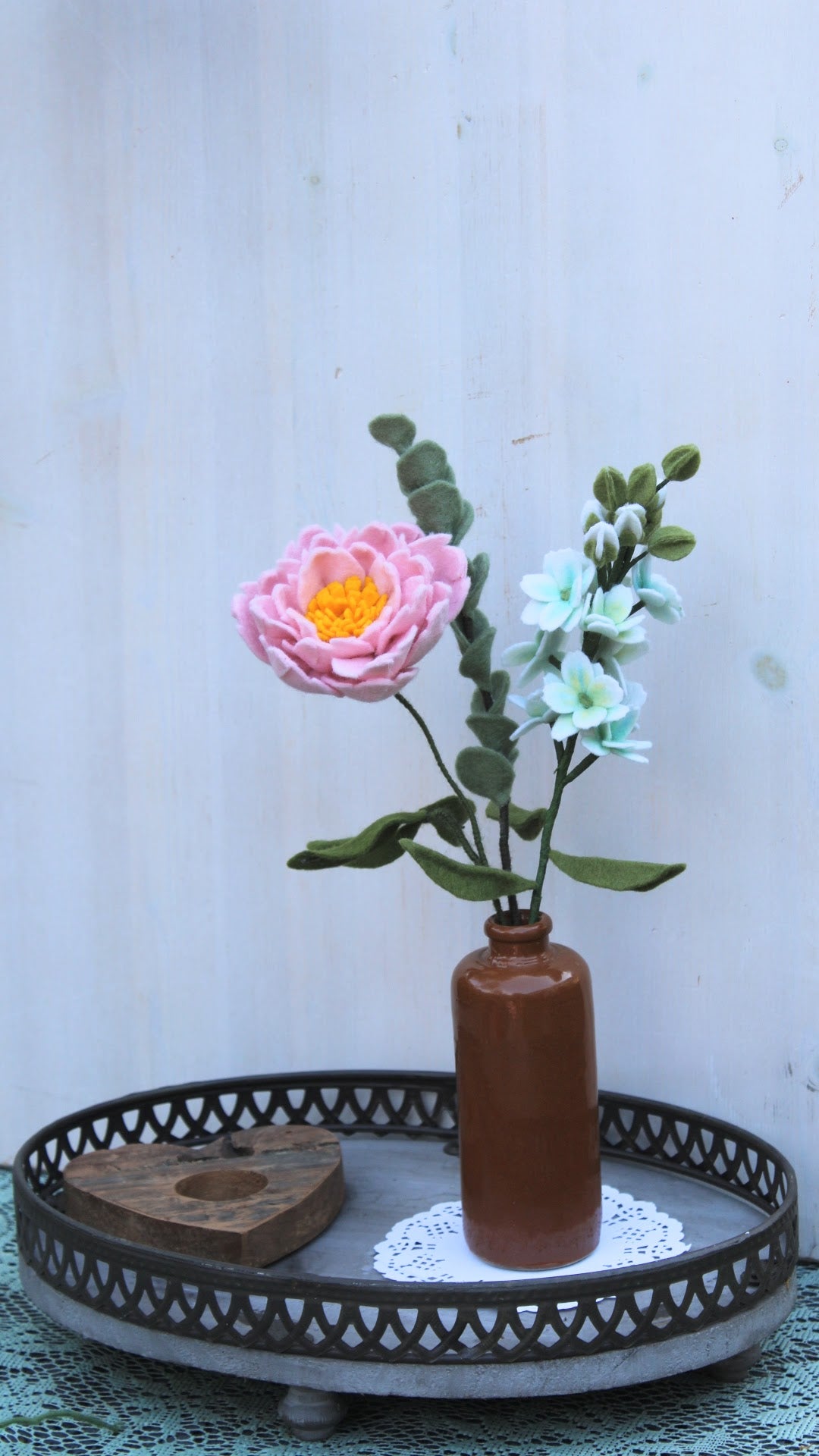 Viltbloemen boeket met een pioenroos, eucalyptus en witte violier in een bruine vaas op een houten dienblad en houten hart met een lichte achtergrond