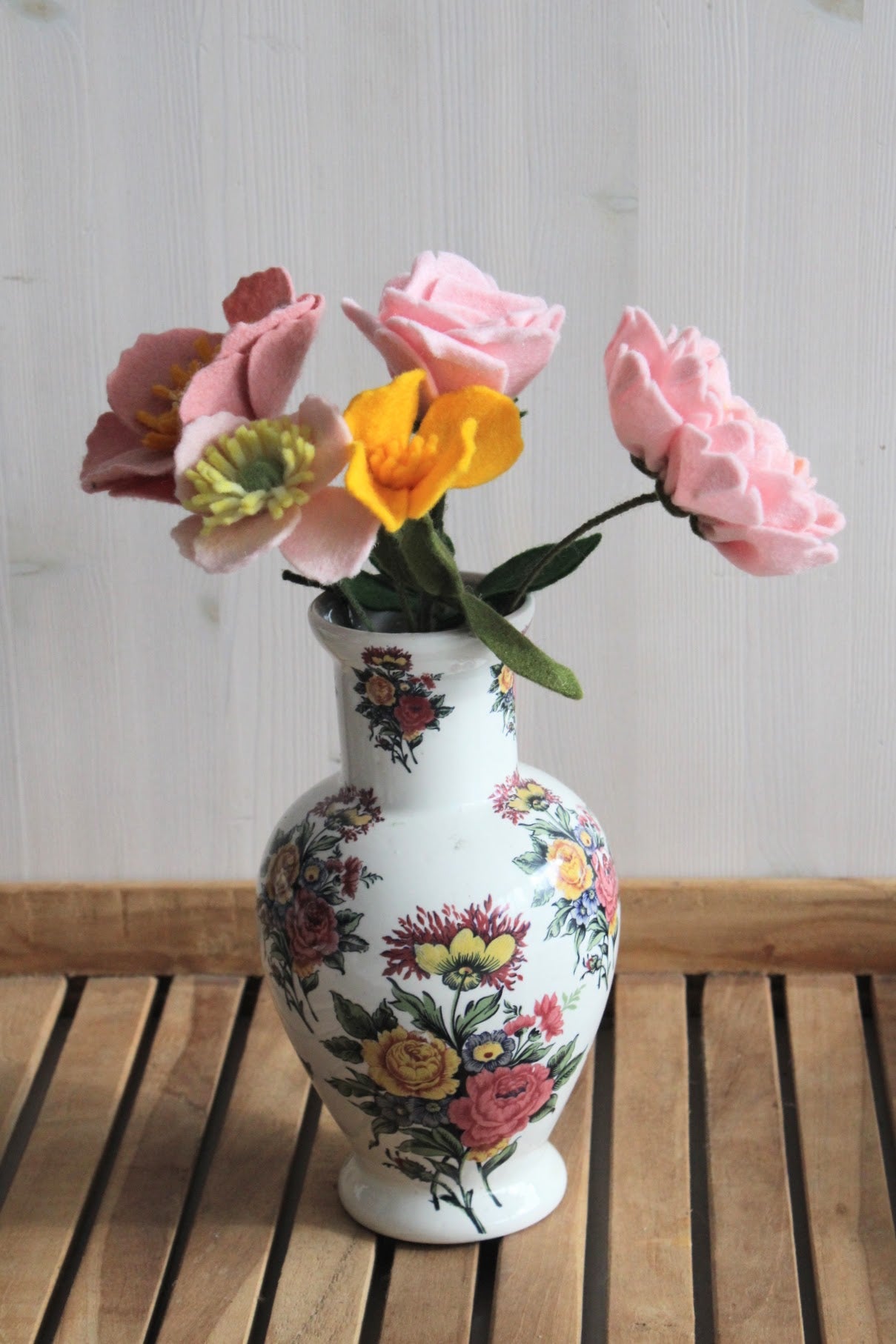 Chinese gebloemde vaas met handgemaakte viltbloemen twee roze anemonen, geel slaapmutsje, roze roos en roze pioenroos op een houten ondergrond