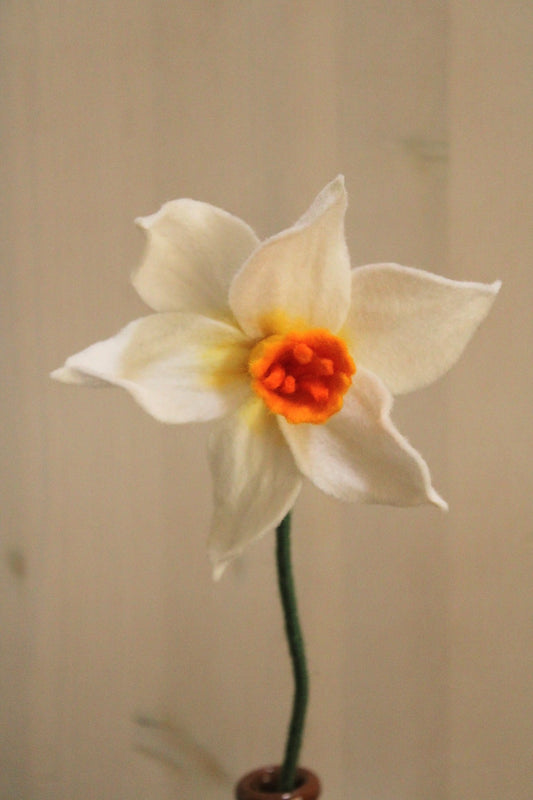close-up van een hangdmaakte vilten wit met gele narcis op een hoge steel met een lichte achtergrond