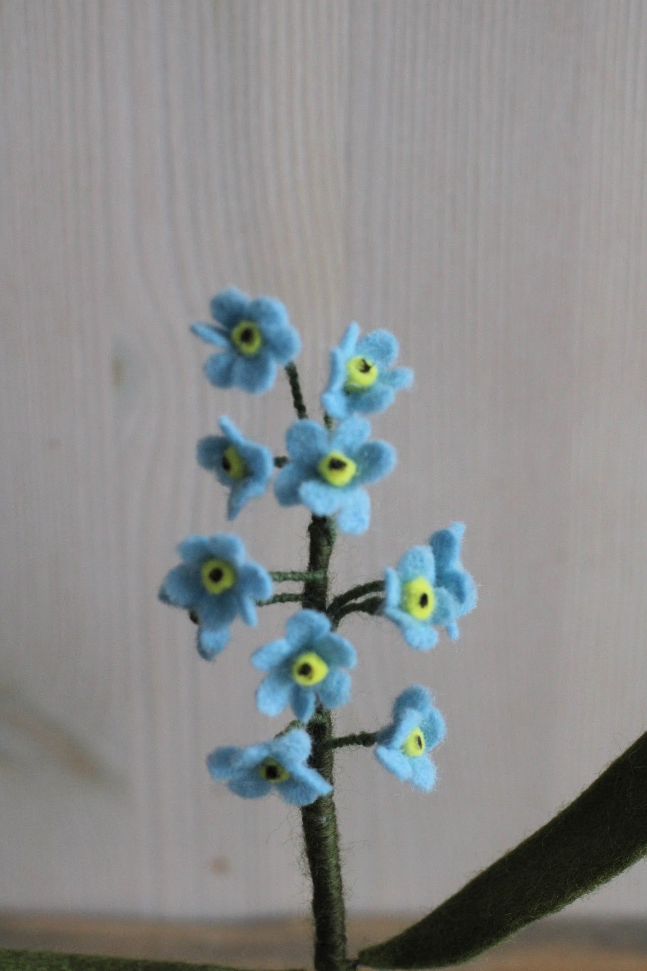Handgemaakte vilten vergeet me nietje met blauwe bloemetjes en een geel hartje, op een korte steel bekleed met groene wol en twee blaadjes. Perfect als duurzame decoratie of als onderdeel van een viltbloemenboeket