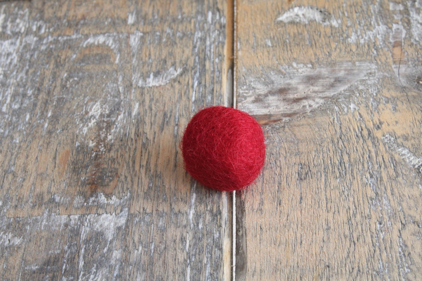 donkerrood viltballetje op een rustiek houten oppervlak. kan gebruikt worden voor hart van viltbloemen of als knutselproject