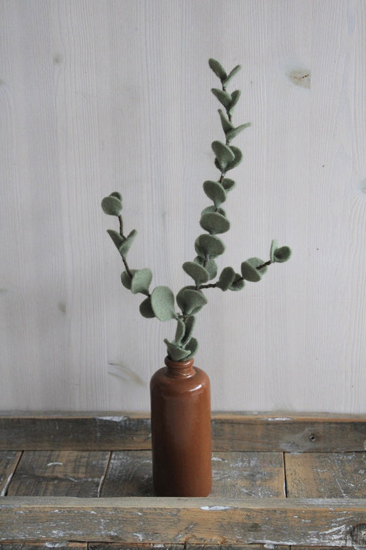 handgemaakte dubbele eucalyptustak van vilt in bruine vaas op houten blad met lichte achtergrond