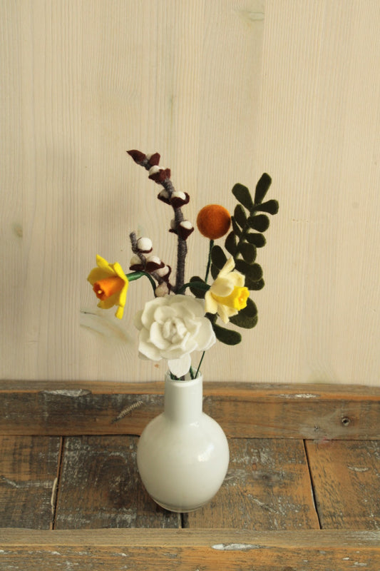 Bolvormig wit glazen vaasje perfect voor kleine viltbloemen, witte bloem, narcisjes, craspedia, wilgenkatjes en groen blad op een houten ondergrond