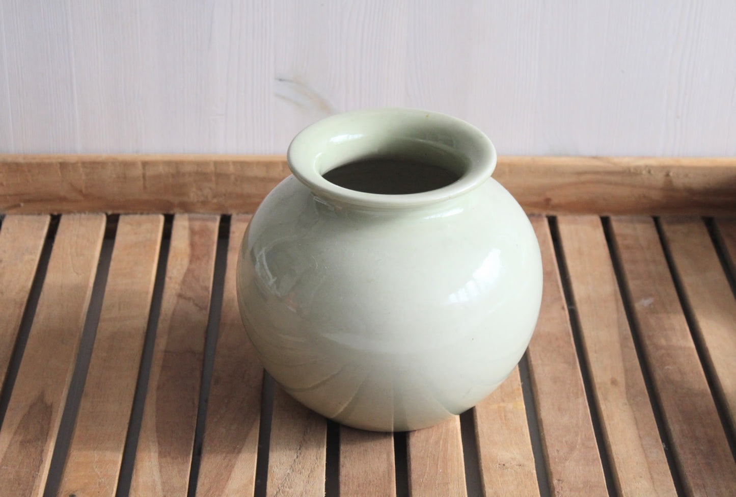 beige-grijze bolvormige vaas om viltbloemen in te zetten, op een houten ondergrond