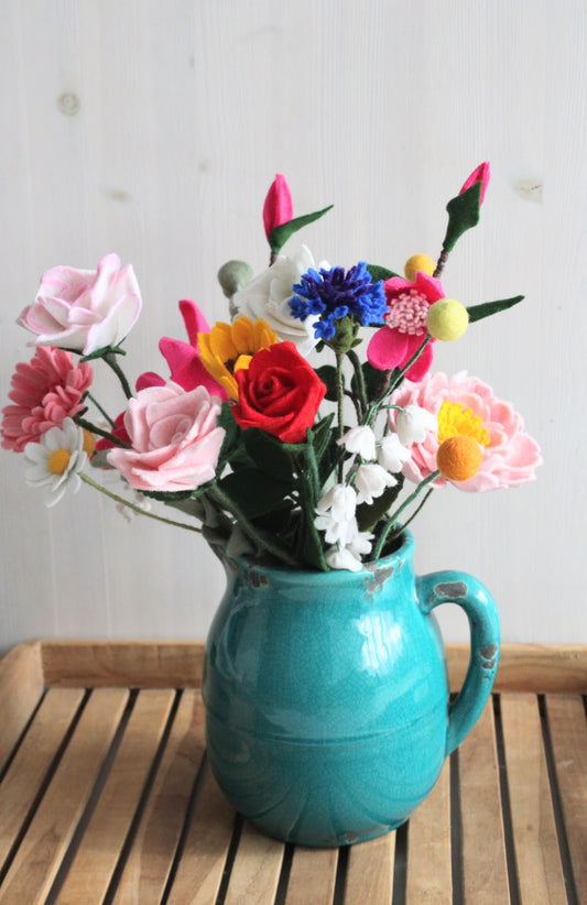 Handgemaakt vilten bloemen boeket als decoratie in een turquoise keramieken waterkan op een houten dienblad