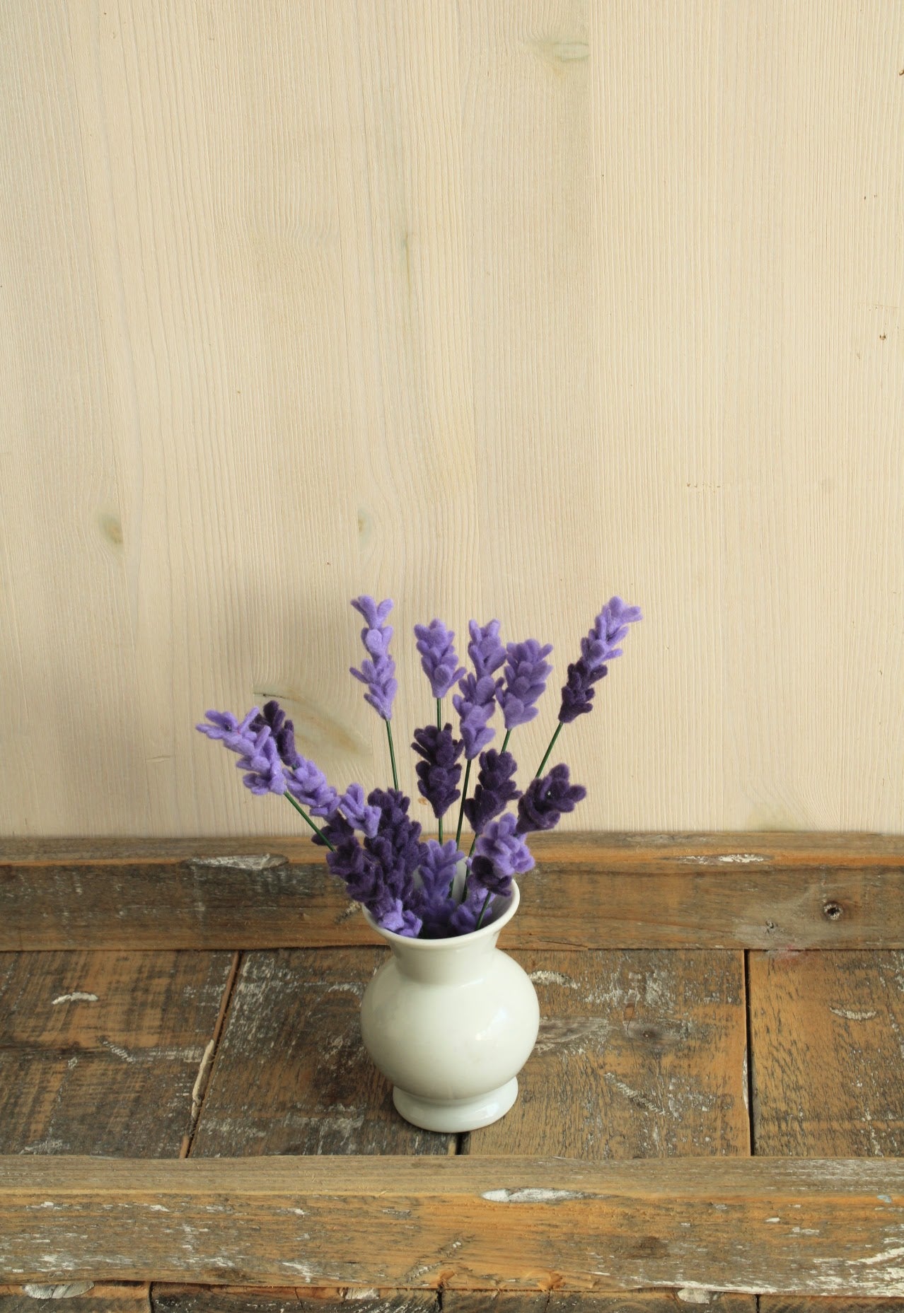 Klein wit vaasje met smalle opening perfect voor handgemaakte viltbloemen, zoals deze paarse lavendel op een rustieke houten ondergrond