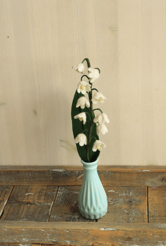 Handgemaakt vilten lelietje van dalen in een blauw vintage vaasje op een houten plank