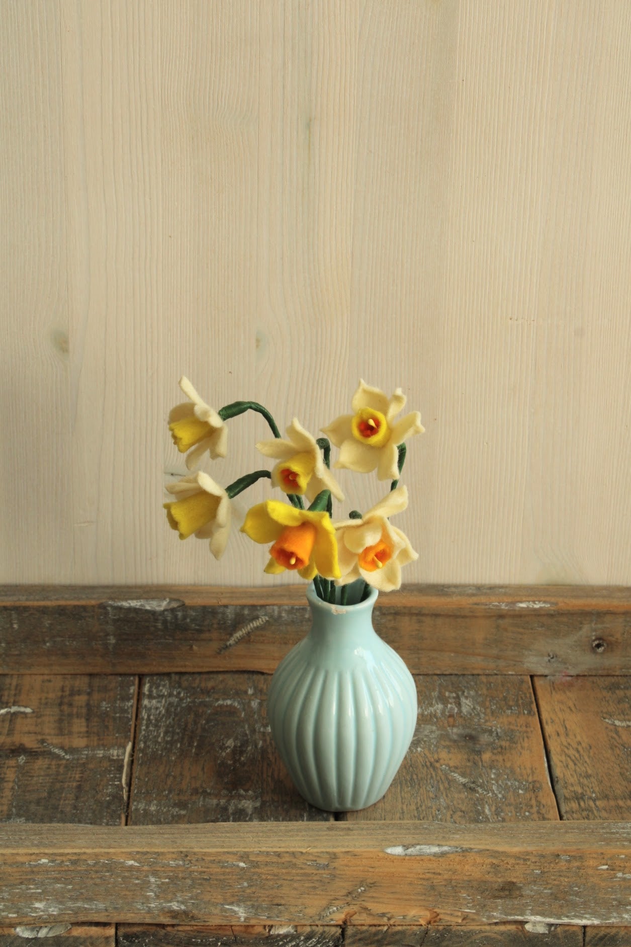 Handgemaakt boeketje met 6 mini Narcisjes in de kleuren wit, geel en donkergeel in een blauw vintage keramieken vaasje op een houten ondergrond