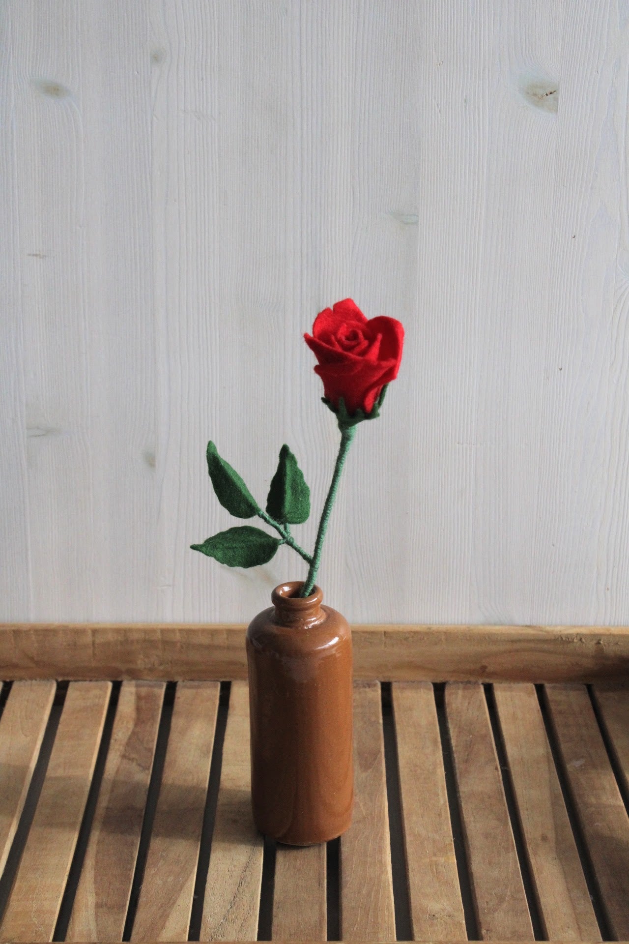 Rode vilten roos met blad, handgemaakt, staat in fles op een houten ondergrond