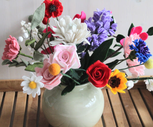 Uitbundig boeket van handgemaakte vilten bloemen in een bolvormige vaas rozen in rood, roze en wit; chrysant; klaprozen; lelietjes-van-dalen; lampionplantjes; zonnebloem; korenbloem; vergeet-mij-nietjes en diverse andere bloemen en groen.