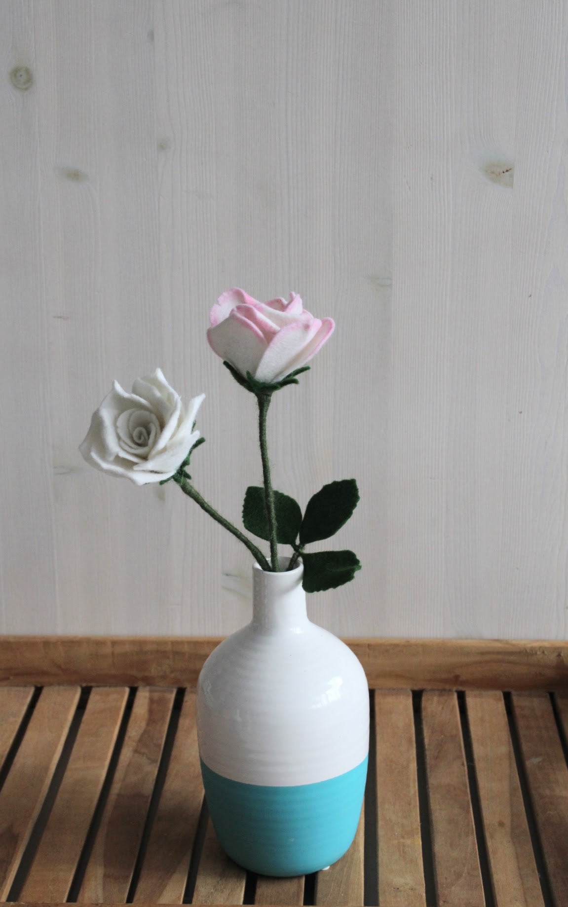 twee rozen van vilt, handgemaakt, in de kleur wit in een wit turquoise vaas flesvorm, op een houten ondergrond