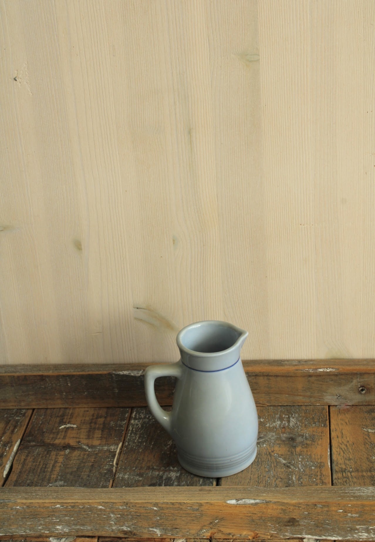 Rustieke blauw-grijze porseleinen kan met handvat en subtiele blauwe lijn, geplaatst op een houten ondergrond