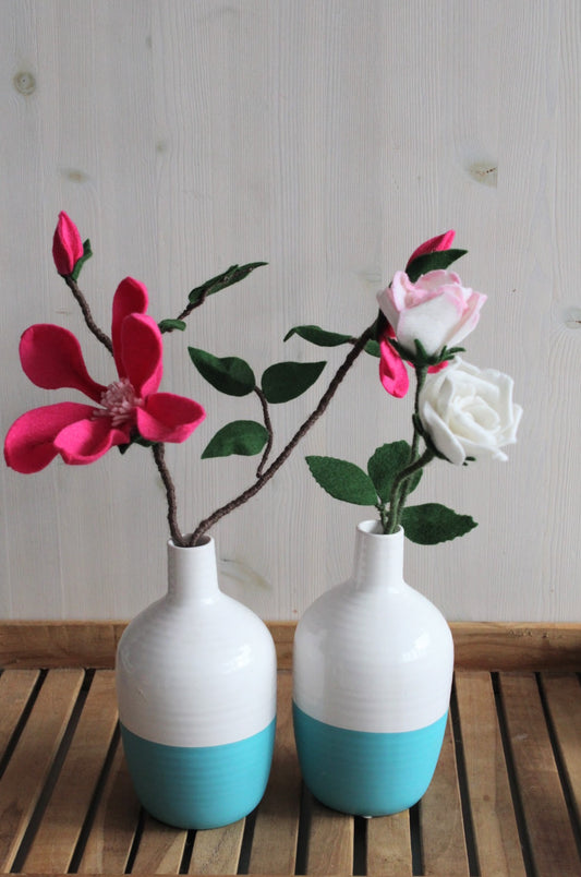 twee wit-turquoise vazen met roze magnolia en twee rozen op een ondergrond van hout