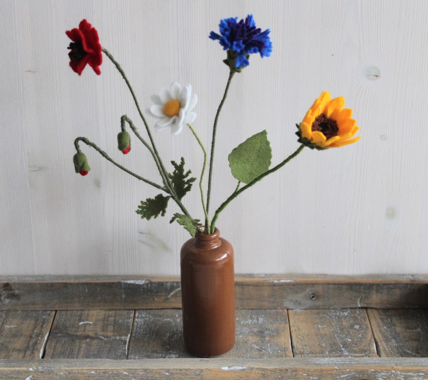 Vilten bloemen veldboeket als decoratie. Handgemaakte zonnebloem, korenbloem, klaproos en margriet van vilt in bruine vaas op een houten achtergrond.