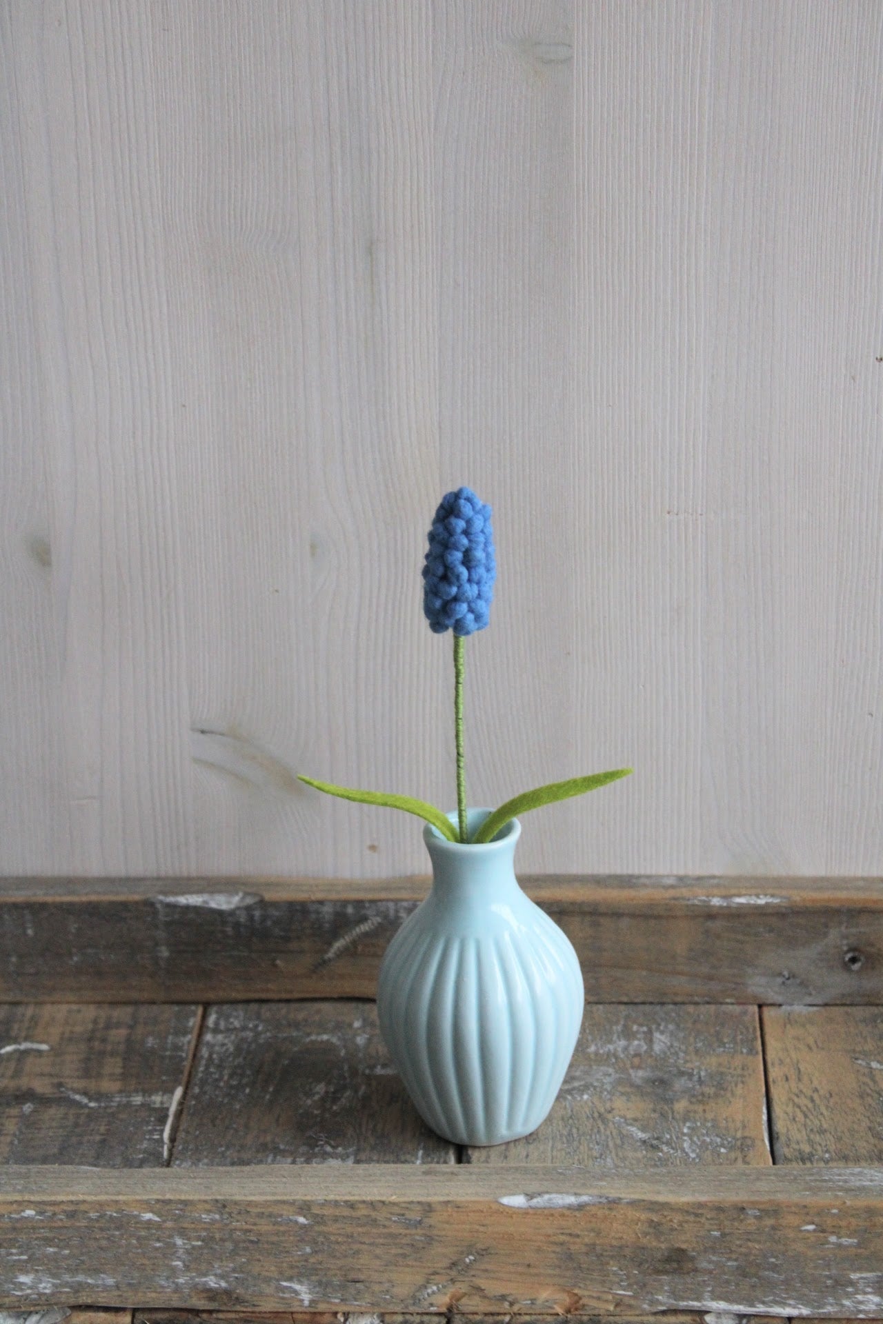 Vilten blauw druifje handgemaakt in een blauw vaasje als lente decoratie op een rustieke houten ondergrond