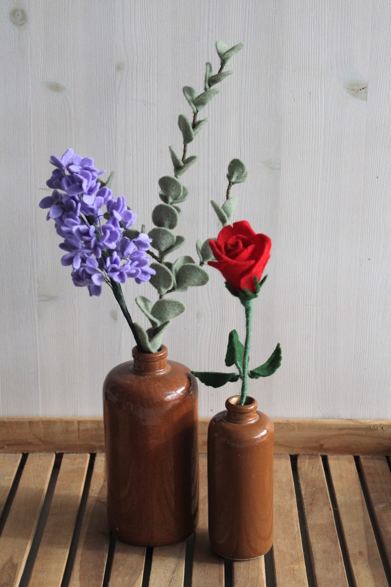 handgemaakte Viltbloemen in jeneverfles, blauwe hortensia, rode roos, eucalyptustak als decoratie op houten ondergrond