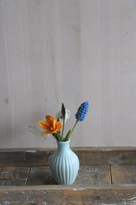 Vilten voorjaarsboeketje met krokus, blauw druifje en sneeuwklokjes als decoratie in een blauw vaasje met houten ondergrond