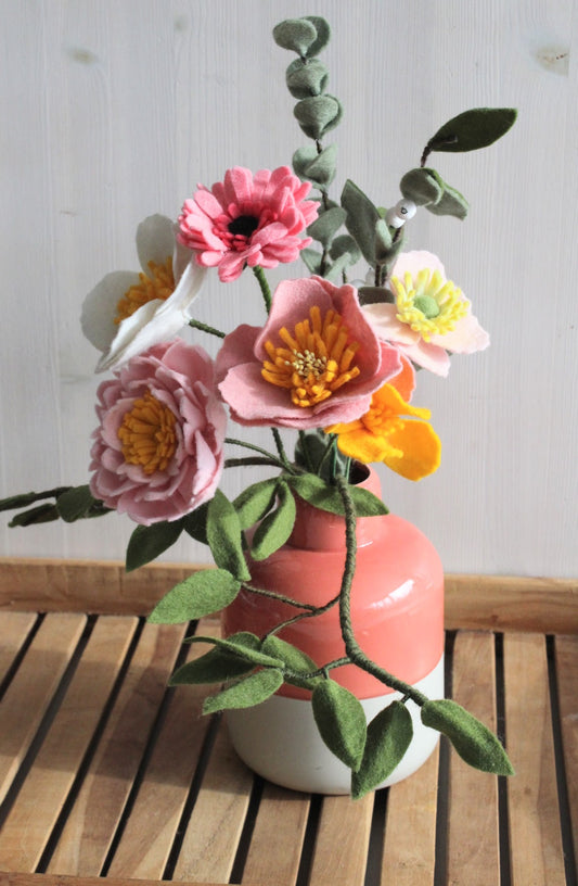 Fleurig gemengd handgemaakt boeket viltbloemen, 3 anemonen, roze gerbera, roze pioenroos, geel slaapmustje met olijftak, eucalyptus en lauriertak in vaas op houten ondergrond