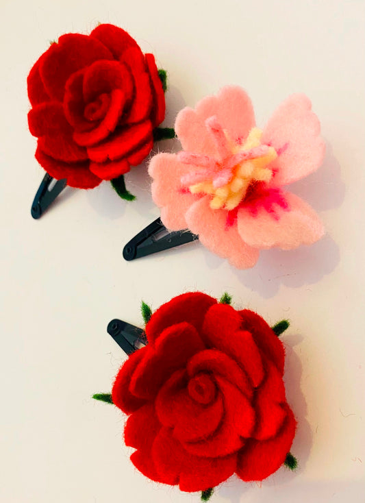 Haarspelden met handgemaakte vilten bloemen: een paar rode rozen en een roze hybiscus op een lichte ondergrond