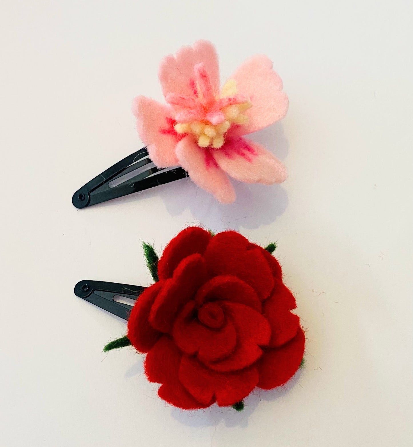 Haarspelden met handgemaakte vilten bloemen, rode roos en roze hybiscus met een lichte achtergrond