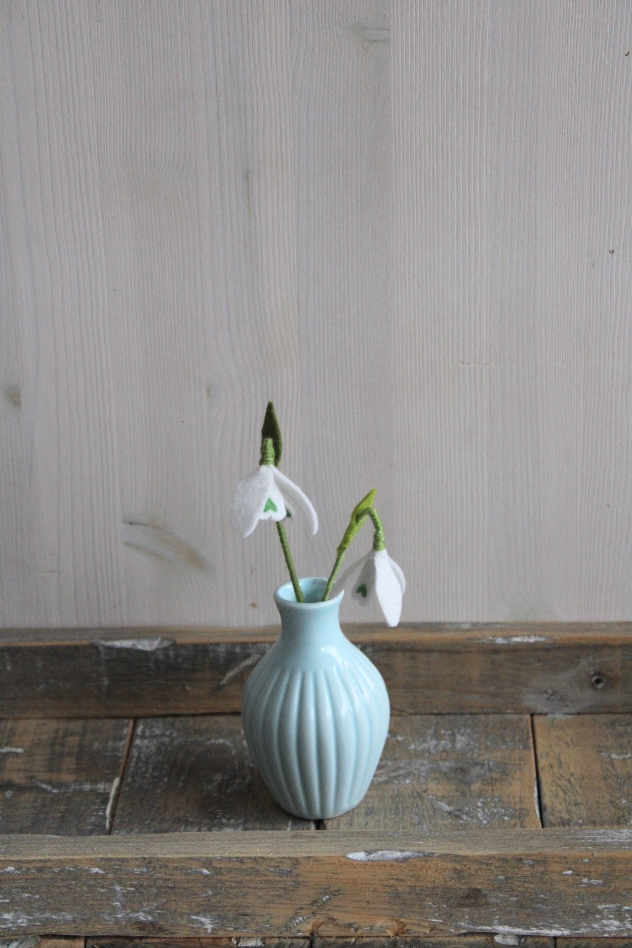 Decoratieve Handgemaakte witte sneeuwklokjes in blauw vaasje met houten ondergrond