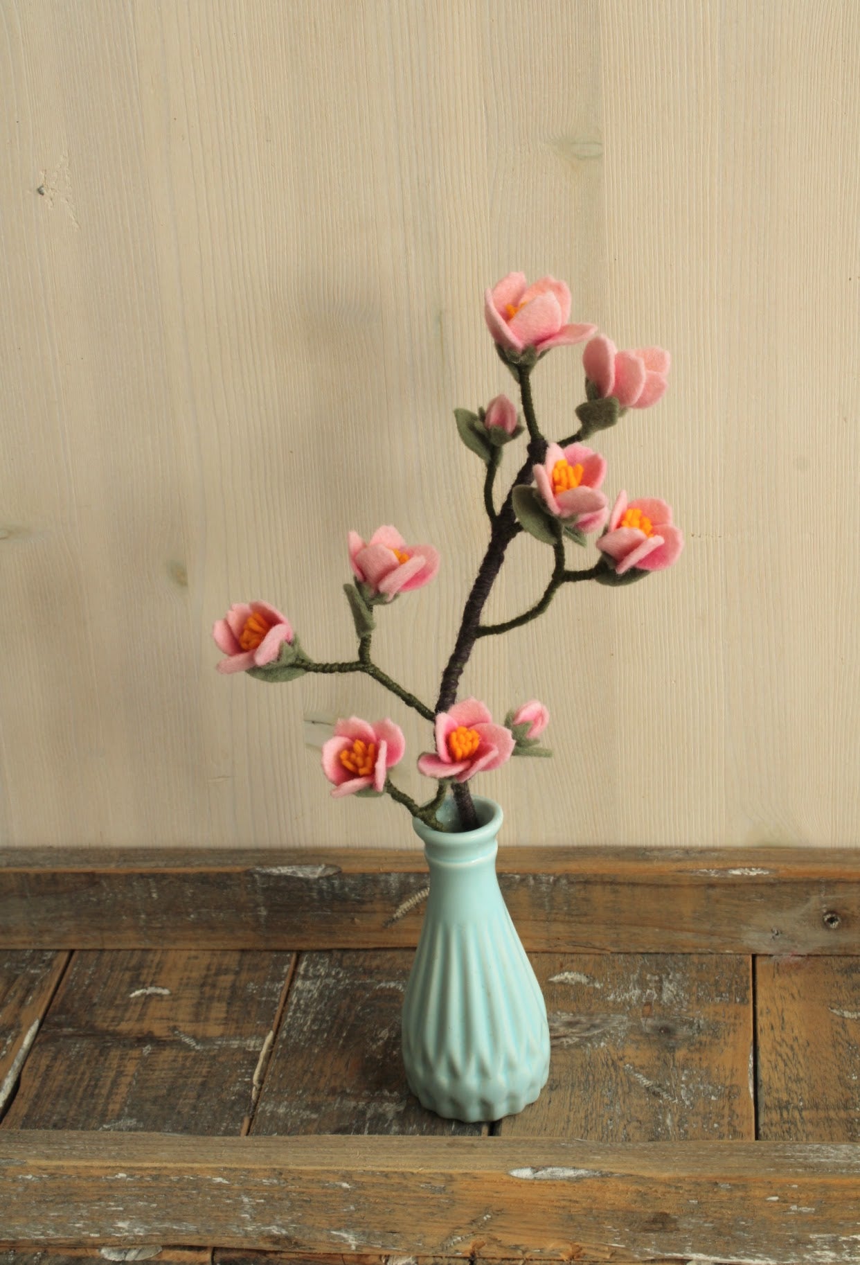 Blauw vintage vaasje met een handgemaakte vilten kersenbloesem tak op een houten ondergrond