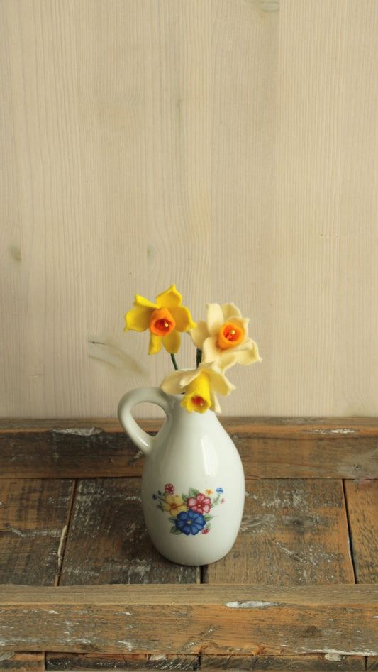 Wit porseleinen kannetje met vilten narcisjes op een houten ondergrond