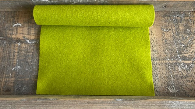 Rolletje wolvilt in de kleur lichtgroen nummer 24 op een houten ondergrond voor het maken van viltbloemen