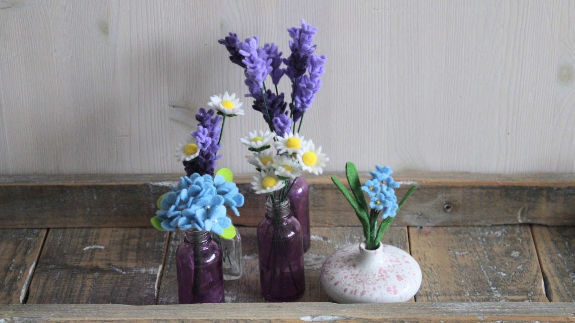 5 mini boeketjes met hortensia/lavendel/madeliefjes/vergeet-me-nietje in verschillende vaasjes op houten ondergrond en lichte achtergrond