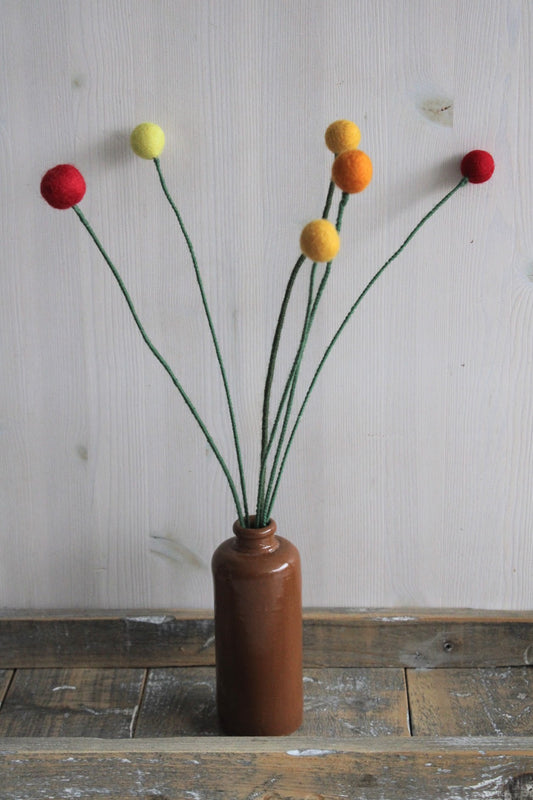 craspedia in een bruine keramieken vaas met houten ondergrond en lichte achtergrond, handgemaakt van viltbolletjes en ijzerdraad bekleed met wol in meerdere kleuren verkrijgbaar geel rood oranje