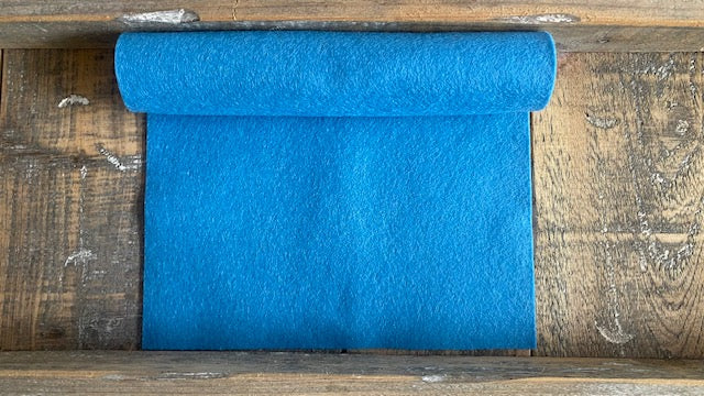 Rolletje wolvilt in de kleur lichtblauw nummer 36 op een houten ondergrond voor het maken van viltbloemen