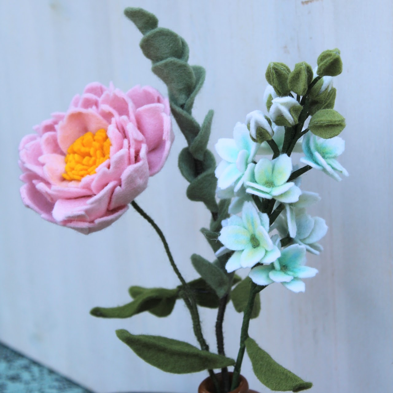 Viltbloemen boeket close up met een pioenroos, eucalyptus en witte violier in een bruine vaas op een houten dienblad en houten hart met een lichte achtergrond