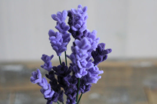 Handgemaakte vilten lavendel als paarse decoratie op een rustieke houten plank.

