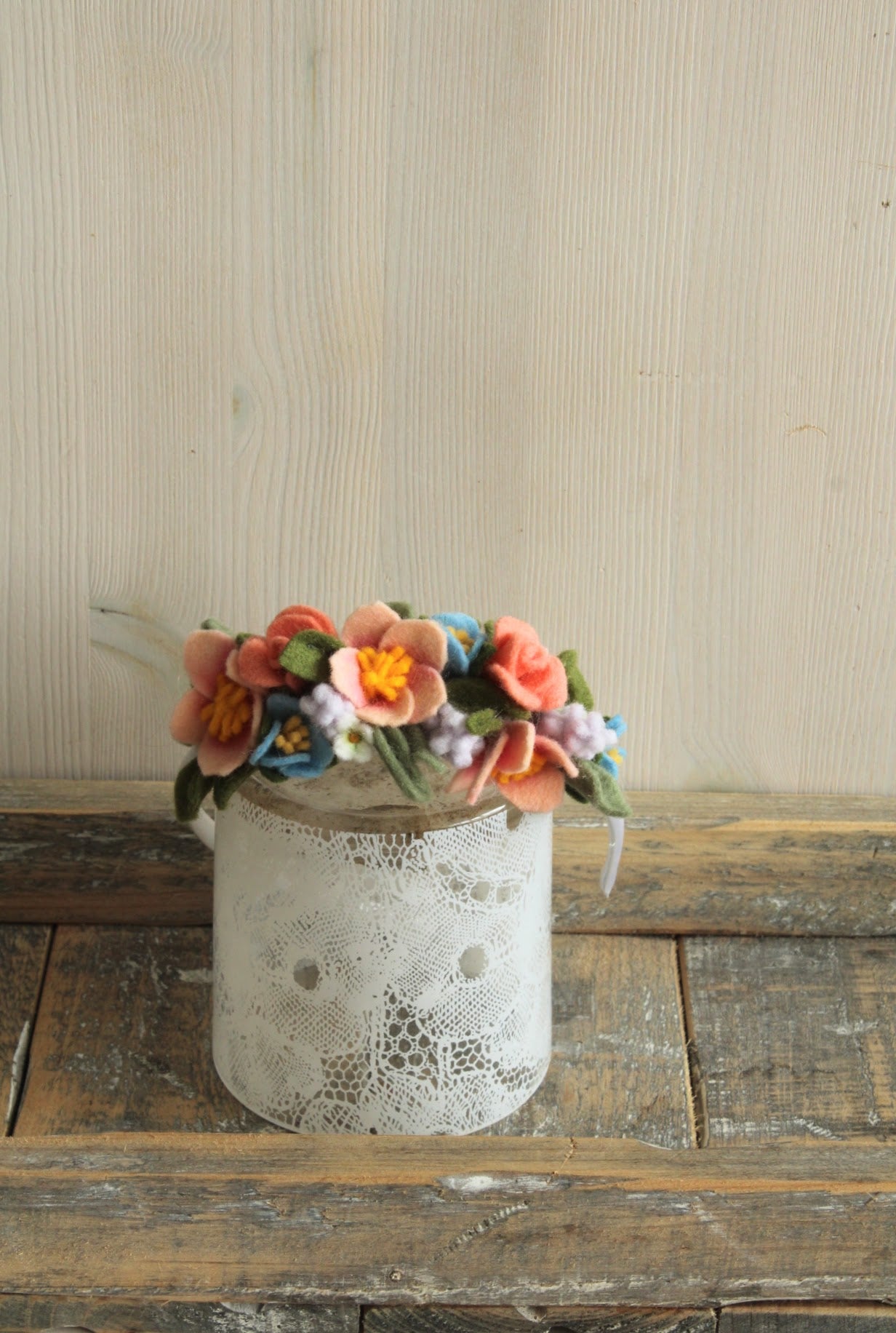 Haarband met viltbloemen op een kanten glaasje op een rustieke houten ondergrond