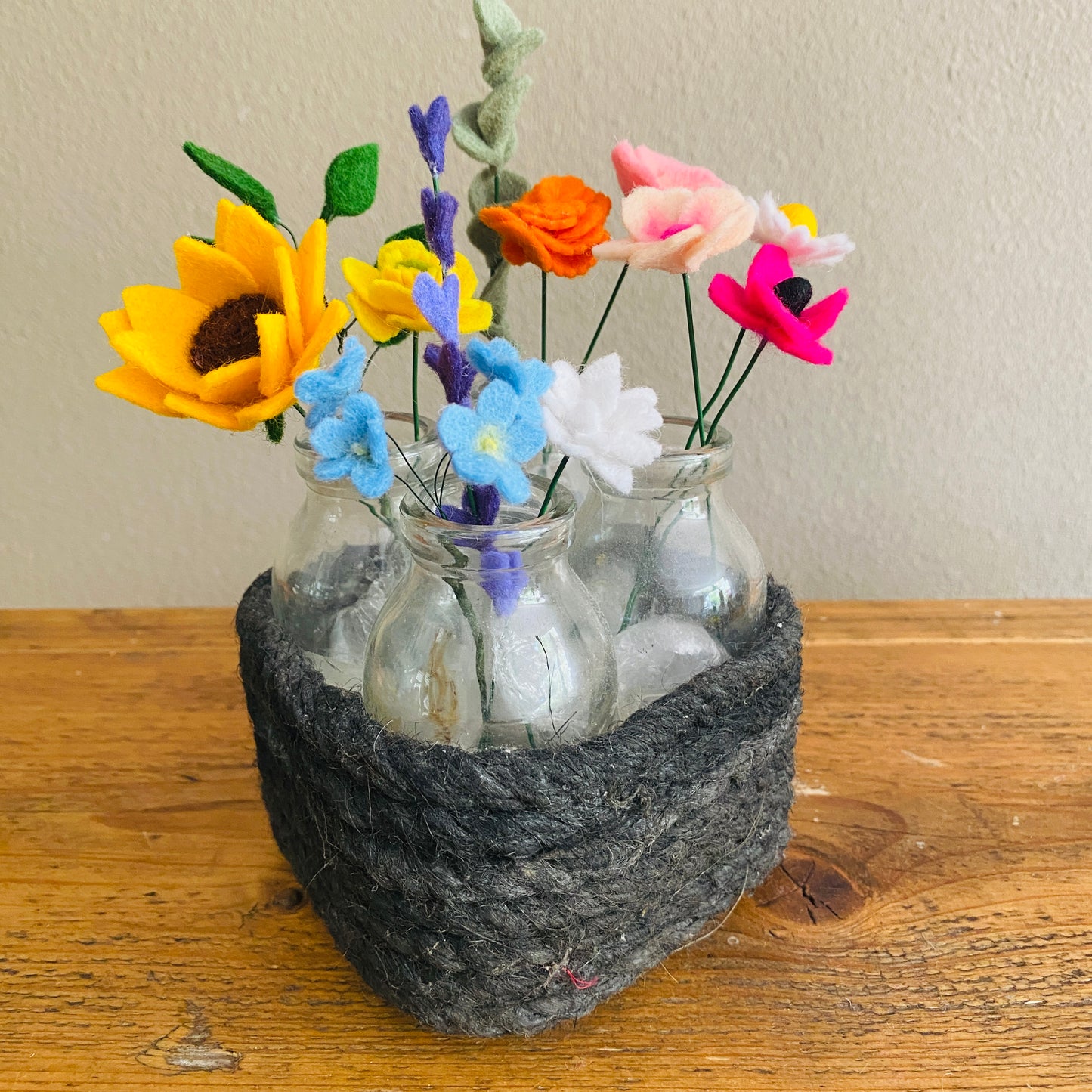 Kleine handgemaakte viltbloemen in een mandje met vaasjes