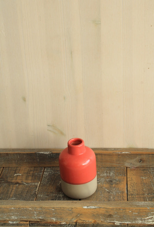 Keramisch vaasje met een moderne tweekleurige afwerking: een matte beige onderkant en een glanzende koraalrode bovenkant, ideaal voor viltbloemen op een  houten rustieke plank